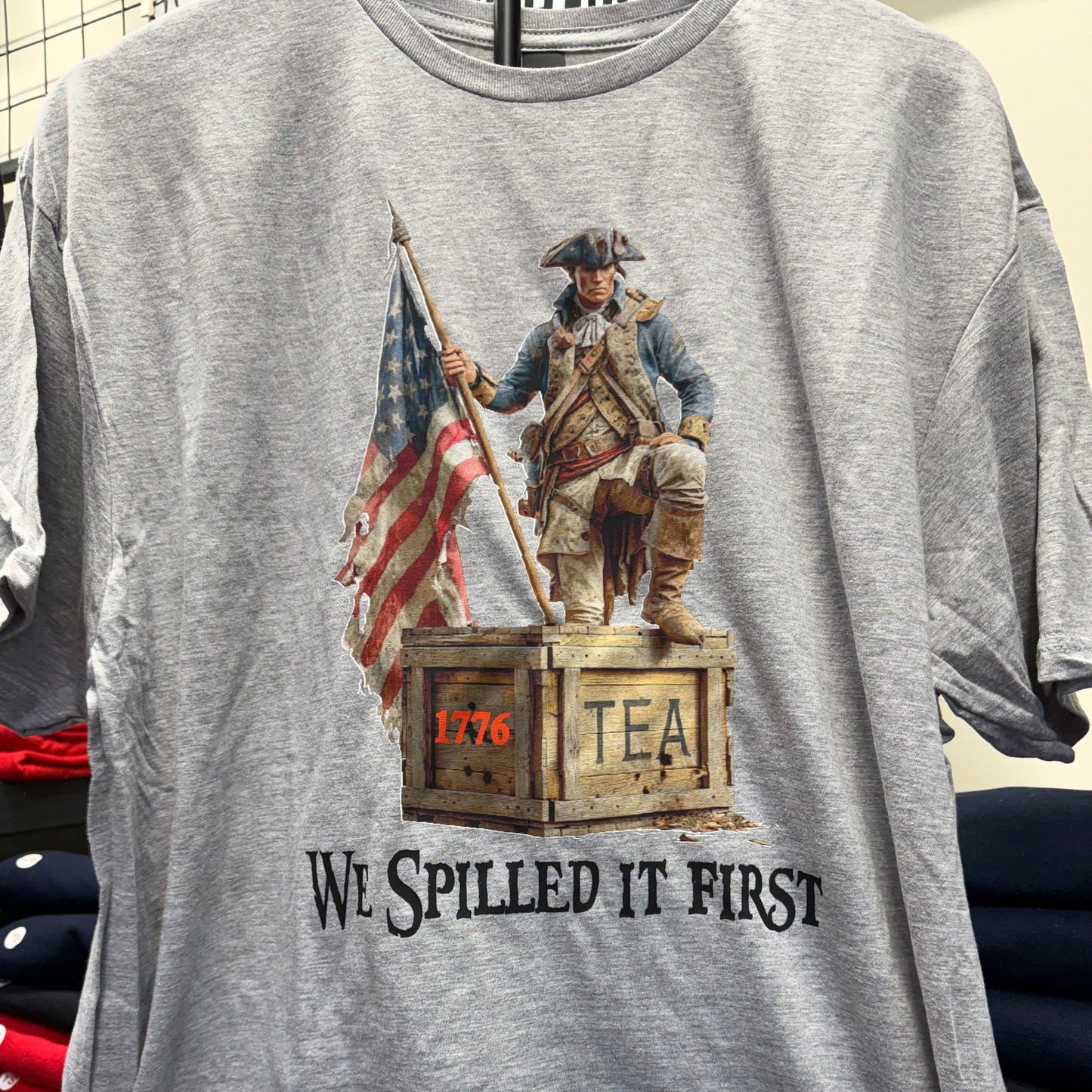 Gray t-shirt with American Revolution-themed graphic and text on a table.